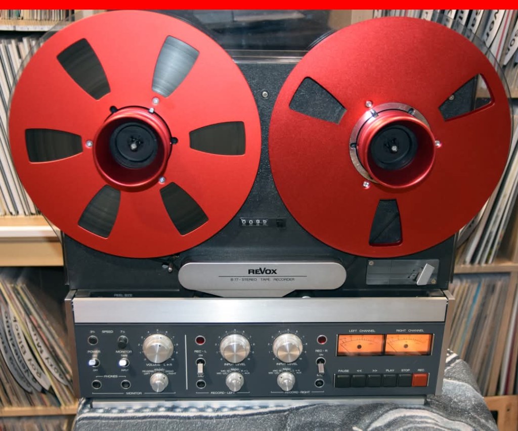 Ein Revox B77 Stereo-Tonbandgerät mit roten Spulen und einem Bedienfeld für Aufnahme und Wiedergabe.