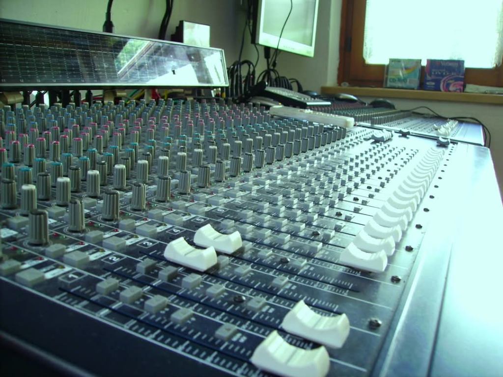 Nahaufnahme eines Mischpults mit vielen Reglern und Knöpfen in einem Studio.